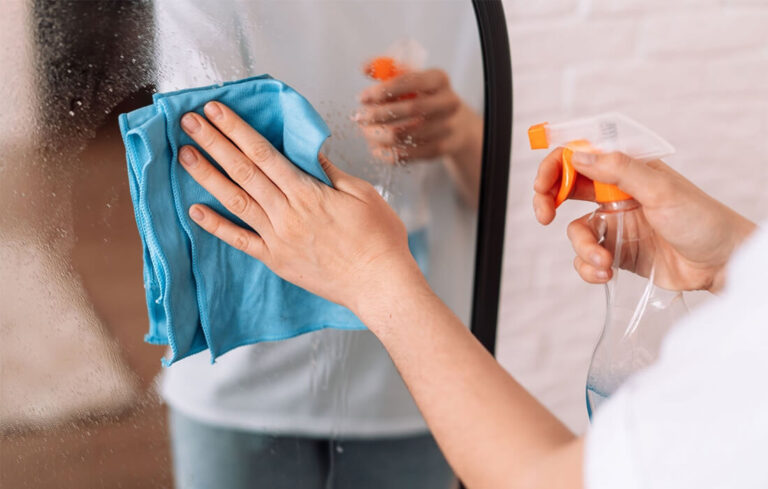 A woman cleaning glass with a microfiber glass cleaning cloth and a water spray